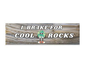 May include: A rectangular bumper sticker with the text "I Brake For Cool Rocks" in white letters. The sticker features a cartoon earth character with arms, legs, and red shoes. The background has a wood grain pattern.