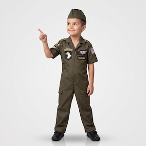 May include: A child's olive green Top Gun costume, including a jumpsuit, cap, and patches. The jumpsuit features patches with the text "Airborne", "Top Gun", and the name "Oliver". The costume includes an American flag patch.