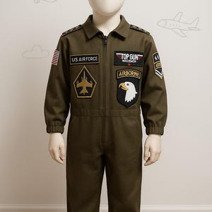 May include: Olive green children's jumpsuit with multiple patches, including "US AIRFORCE", "TOP GUN", and "AIRBORNE". The costume features a zipper closure and long sleeves. The patches include an American flag and military insignia.