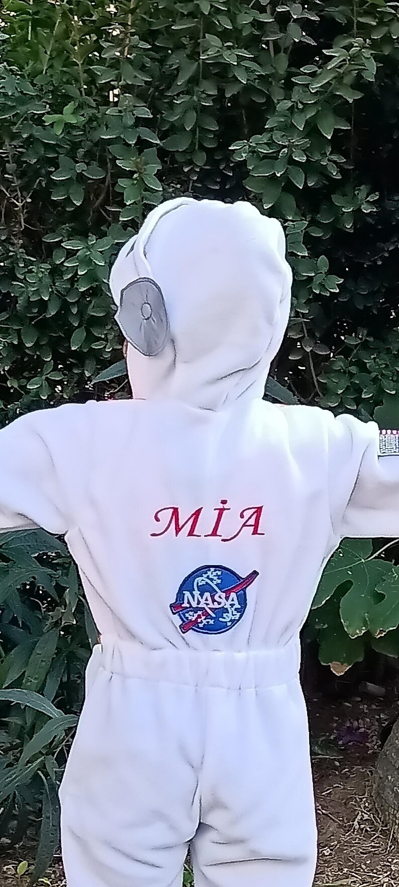 Op de afbeelding: Wit astronaut pak met een NASA-logo en de naam "MIA" geborduurd op de voorkant.