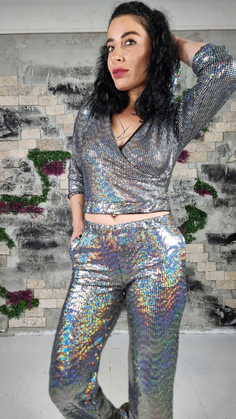 Puede incluir: Un conjunto de top y pantal&oacute;n de lentejuelas plateadas. El top tiene cuello en V y mangas largas. El pantal&oacute;n es de cintura alta y tiene pierna recta.