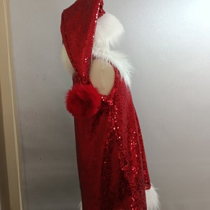 May include: Red sequined Santa dress with a white fur trim and a matching hood. The hood has a white fur trim and a red pom-pom.