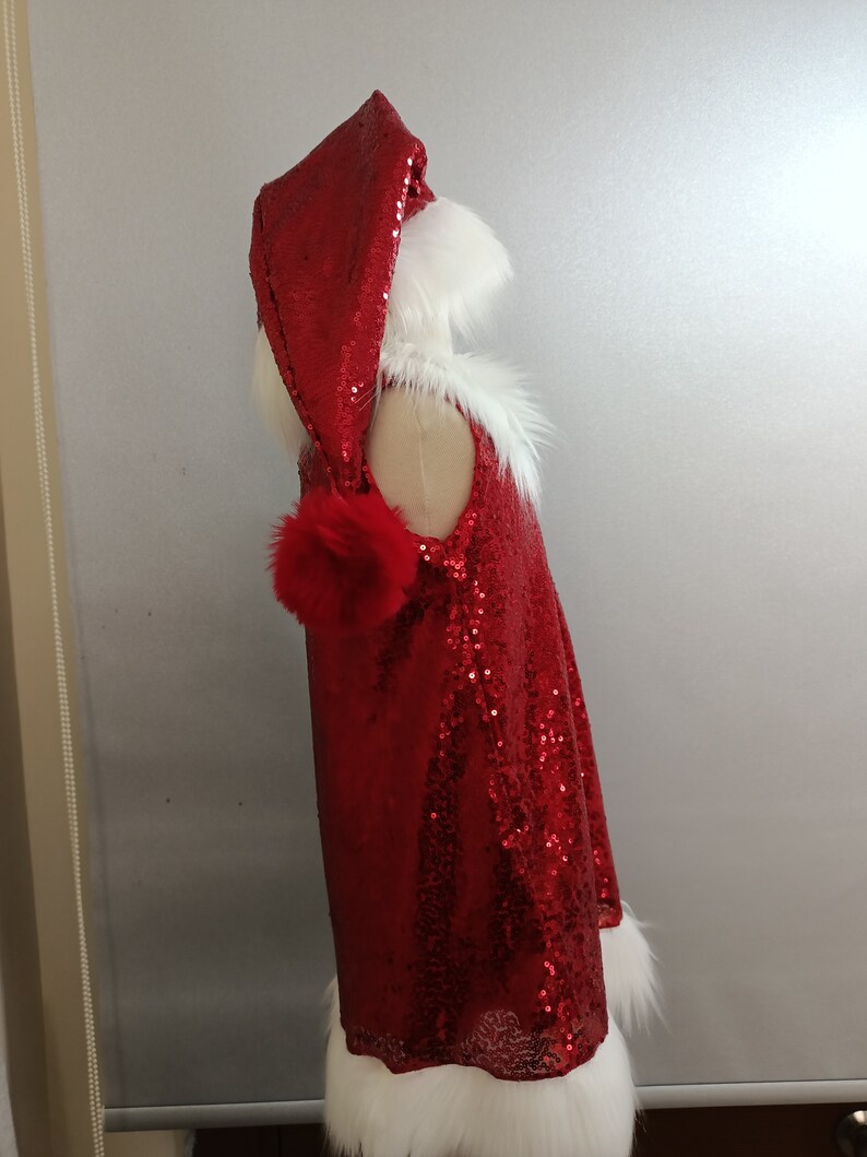 May include: Red sequined Santa dress with a white fur trim and a matching hood. The hood has a white fur trim and a red pom-pom.