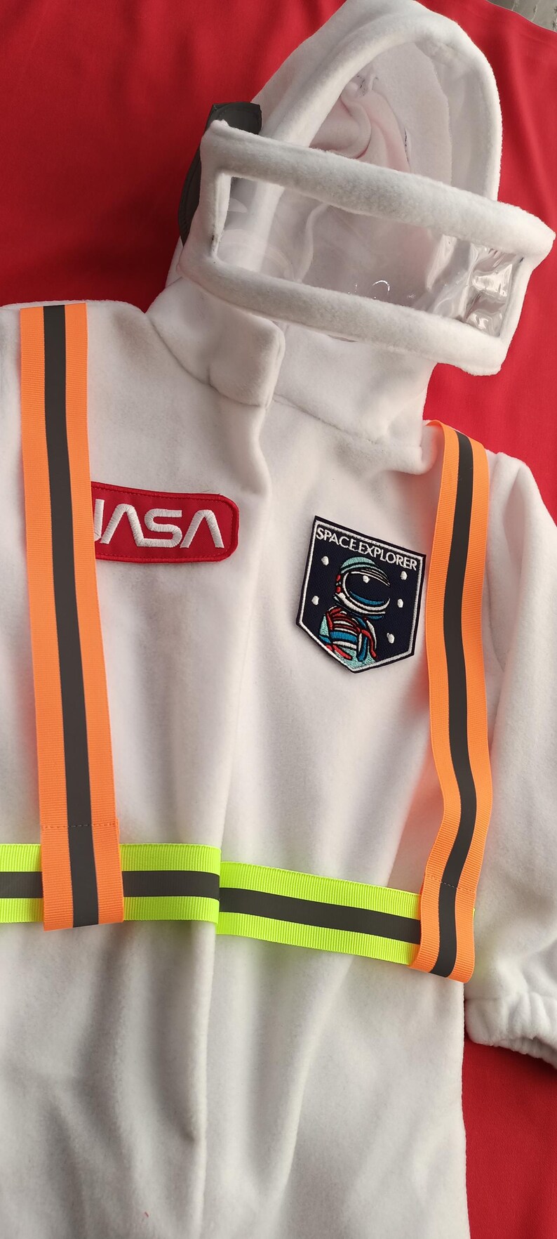Op de afbeelding: Wit astronaut kostuum met oranje en zwarte banden, een NASA-patch en een Space Explorer-patch met een astronaut ontwerp.
