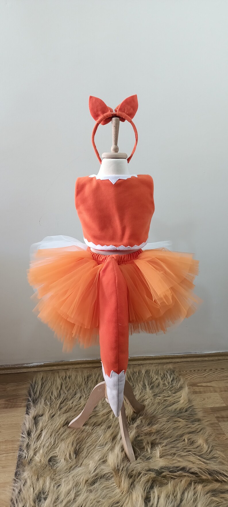 May include: Orange and white fox costume for a child. The costume includes a tutu skirt, a top with a tail, and a headband with fox ears.