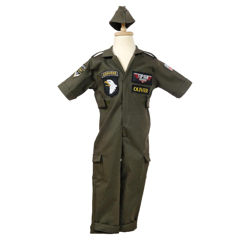 May include: Olive green Top Gun flight suit costume with matching cap. Features embroidered patches including "Airborne", a white eagle, and "Top Gun". The name "Oliver" is embroidered on the chest. Includes two front pockets and a US flag patch.