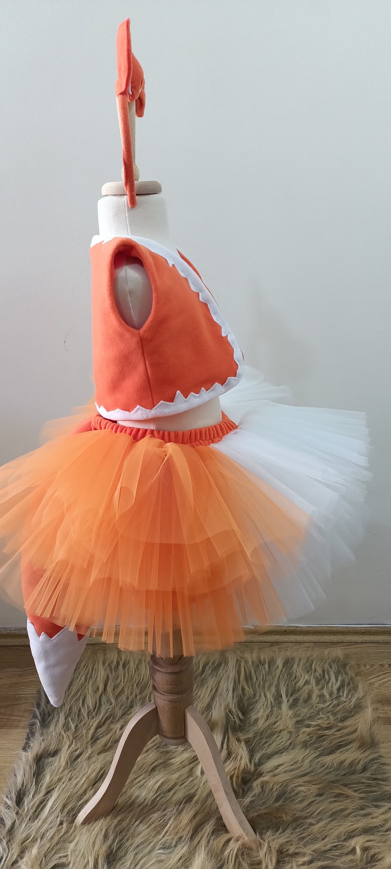 May include: Orange and white fox costume for a baby or toddler. The costume includes a vest, a tulle skirt, and a tail.