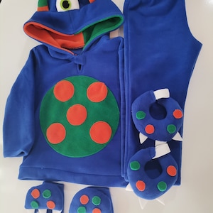 May include: A blue monster-themed costume set for children. The set includes a hooded sweatshirt with a large green and orange circle design, matching pants, and monster feet and hand covers. The hood has a large eye and horns.