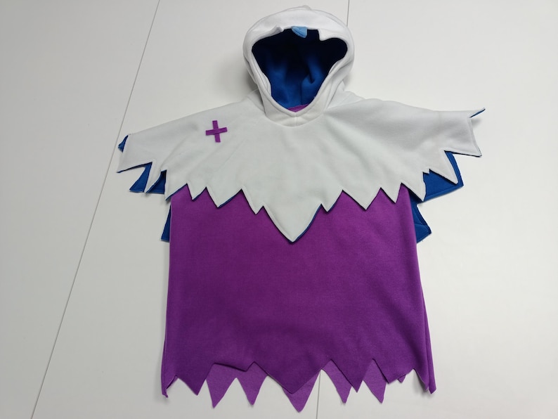 May include: A hooded costume in white, purple, and blue. The costume has a white hood with a blue interior, a white cape with a purple cross, and a purple body with a jagged hemline. The costume is designed to look like a ghost.