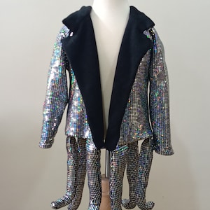 Puede incluir: Una chaqueta plateada con lentejuelas, con cuello negro y mangas largas. La chaqueta est&aacute; en un maniqu&iacute; con seis piernas de lentejuelas.