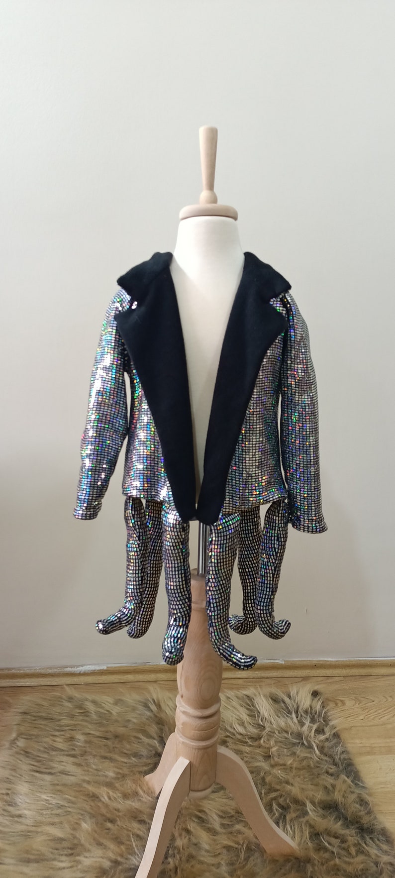Puede incluir: Una chaqueta plateada con lentejuelas, con cuello negro y mangas largas. La chaqueta est&aacute; en un maniqu&iacute; con seis piernas de lentejuelas.