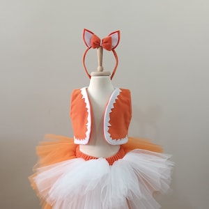 May include: A white and orange tulle tutu skirt with an orange vest and a headband with fox ears. The costume is on a mannequin.