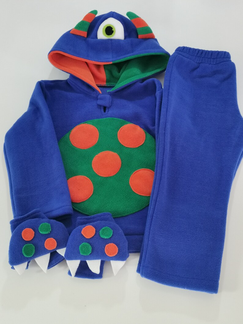 May include: A blue monster-themed fleece outfit, including a hooded sweatshirt, pants, and monster claw mittens. The sweatshirt features a green and orange design with orange spots and a large eye on the hood.