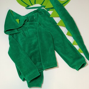 May include: Green dragon costume for kids, featuring a hooded sweatshirt, pants, tail, and wings. The costume is made of soft fleece fabric.