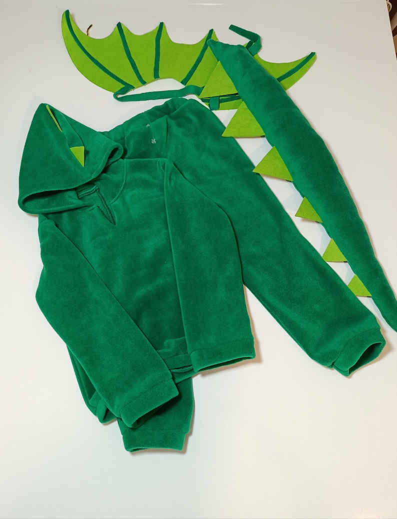 May include: Green dragon costume for kids, featuring a hooded sweatshirt, pants, tail, and wings. The costume is made of soft fleece fabric.