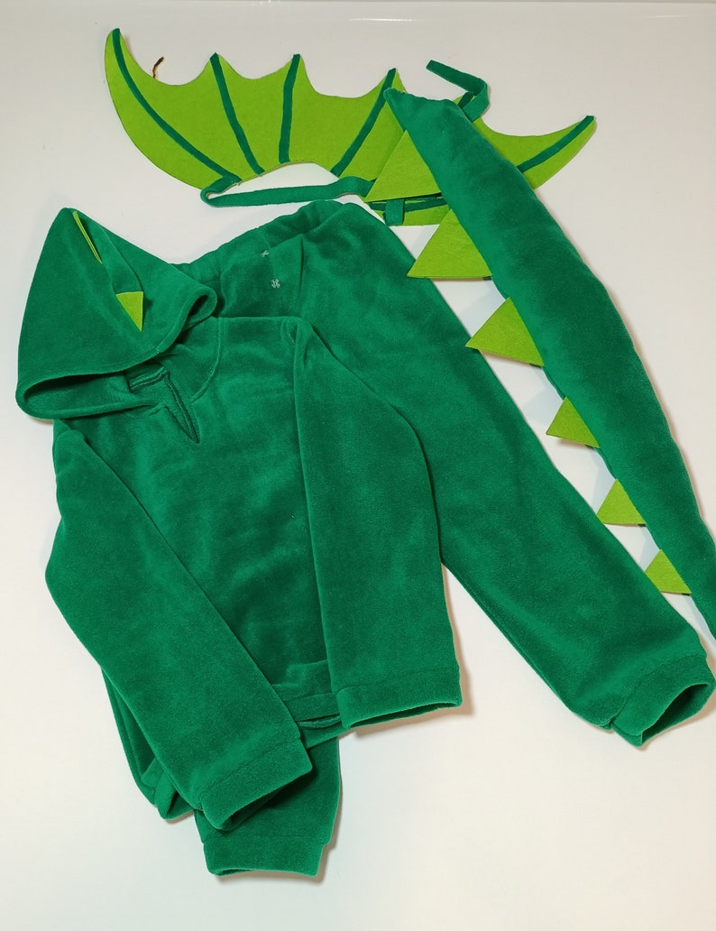 May include: Green dragon costume for kids, featuring a hooded sweatshirt, tail, and wings. The costume is made of soft, plush fabric.