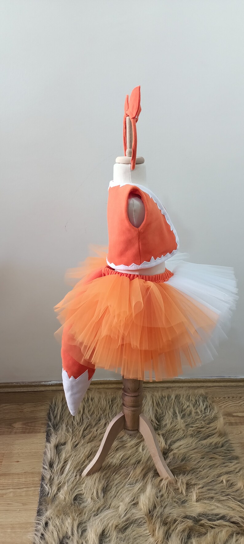 May include: Orange and white fox costume for a child. The costume includes a tulle skirt, a top with a white trim, and a tail.