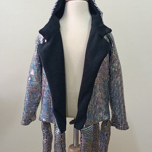 Puede incluir: Una chaqueta con capucha de lentejuelas plateadas con forro negro y ocho largas tentaculos de lentejuelas plateadas unidas a la parte inferior. La chaqueta est&aacute; en un maniqu&iacute; de madera.