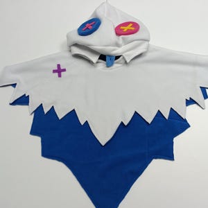 May include: A white and blue costume with a hood. The hood has two circular accents, one blue and one pink. The costume has a jagged edge design and a purple cross accent. The costume is made of soft fabric.