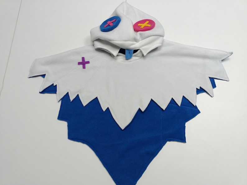 May include: A white and blue costume with a hood. The hood has two circular accents, one blue and one pink. The costume has a jagged edge design and a purple cross accent. The costume is made of soft fabric.