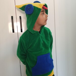 Puede incluir: Una sudadera con capucha verde, amarilla y azul con un dise&ntilde;o de rana en la capucha. La sudadera tiene un bolsillo azul en la parte delantera.