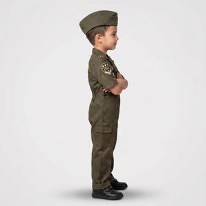May include: A child's olive green military uniform, including a cap, short-sleeved jumpsuit, and black shoes. The uniform features patches on the shoulder and chest. The child has their arms crossed.