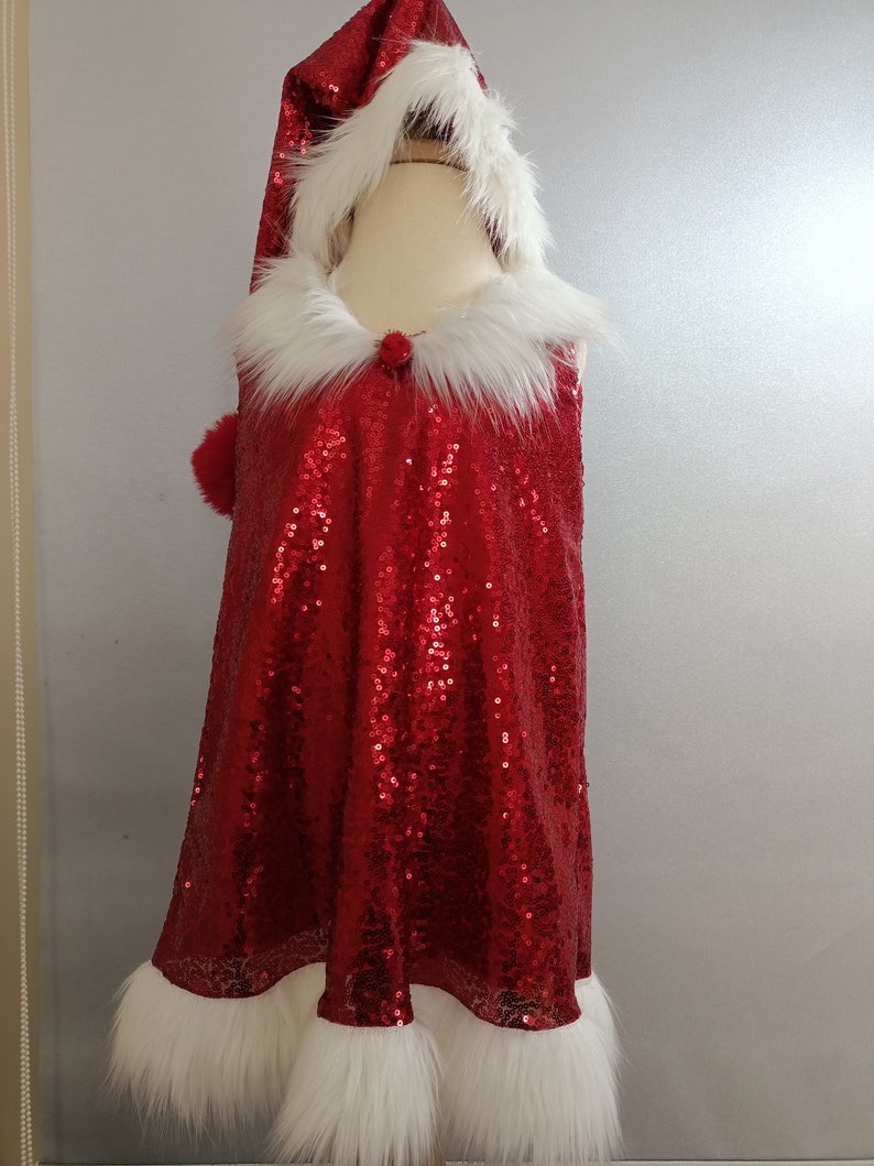 May include: A red sequined Santa dress with a white faux fur trim around the hood, neckline, and hem. The dress has a sleeveless design and a pom-pom on the hood.