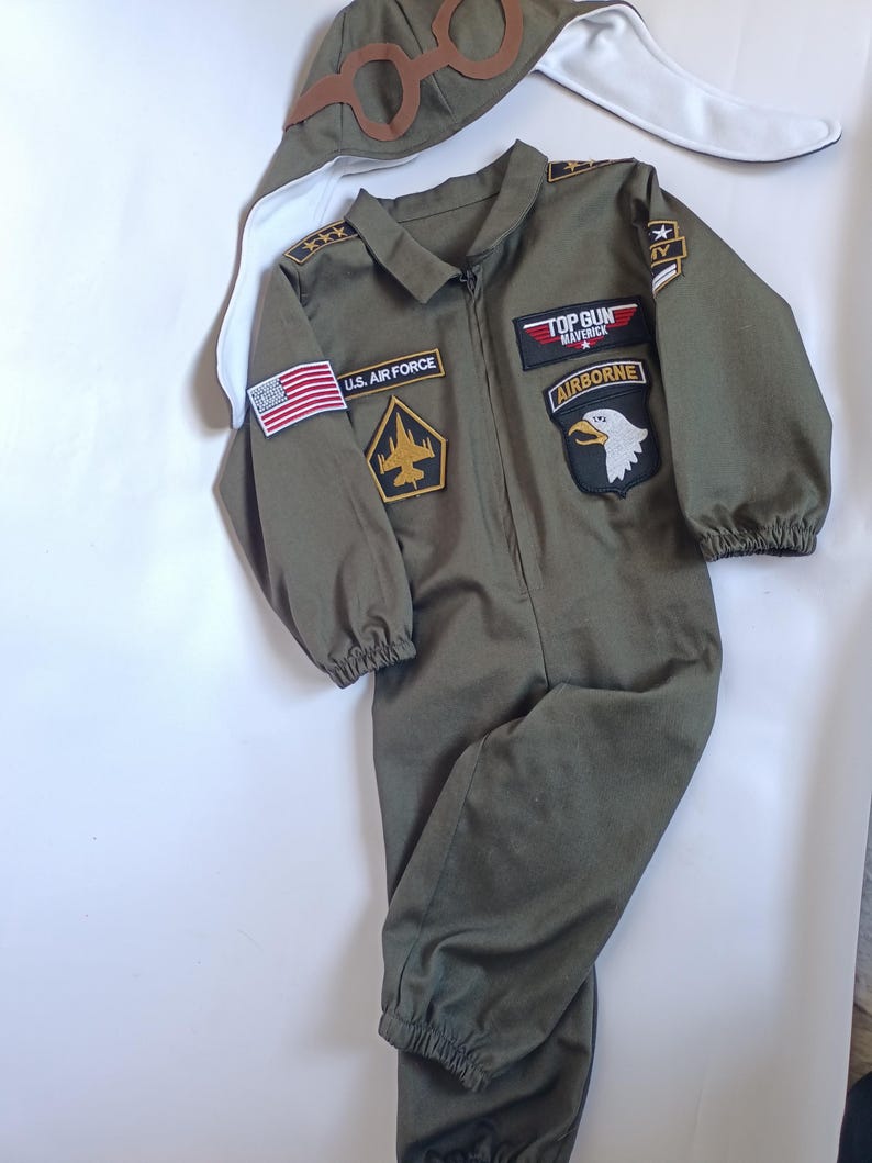 May include: Olive green Top Gun Maverick flight suit with patches, including U.S. Air Force and Airborne. Includes a matching aviator hat with goggles. The jumpsuit has a zipper closure and elastic cuffs at the wrists and ankles.