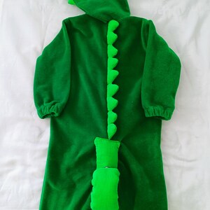 May include: Green dinosaur costume for a child with a large eye on the hood and a tail with spikes.