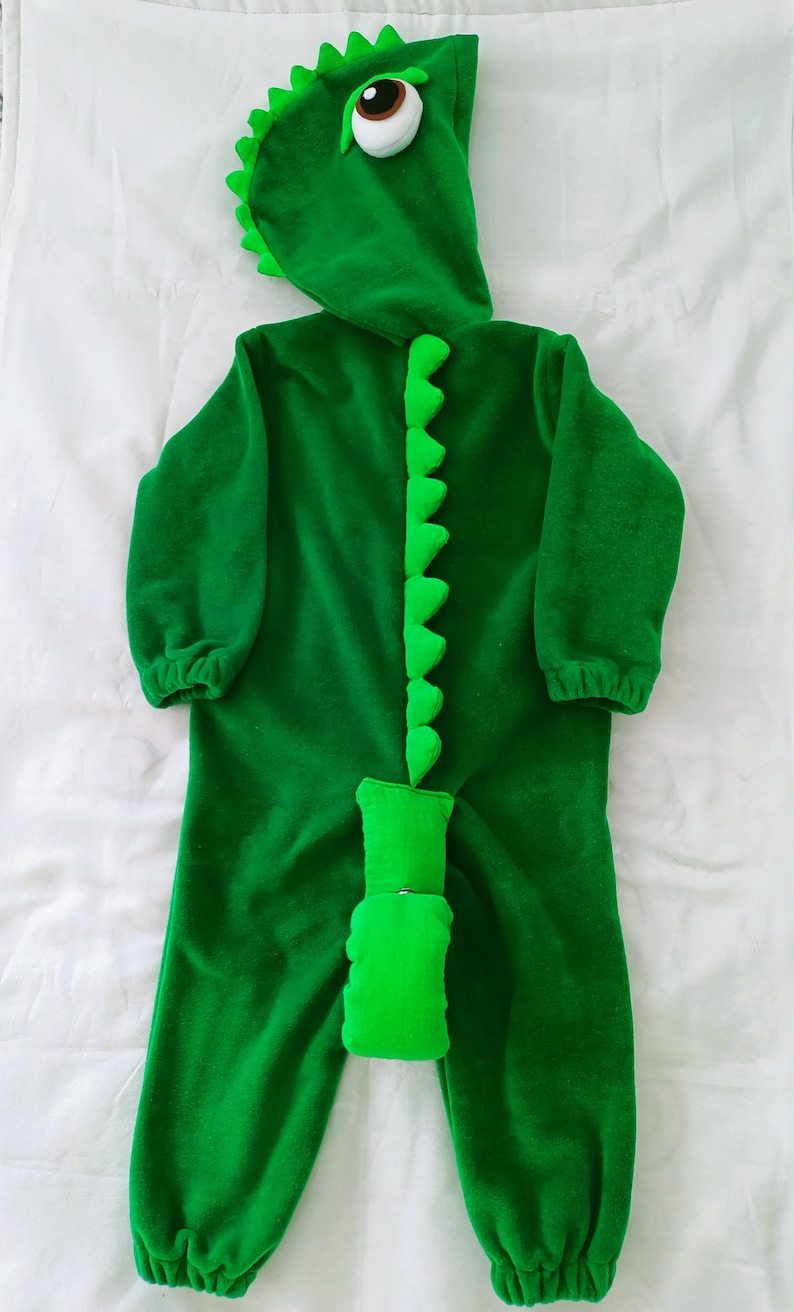 May include: Green dinosaur costume for a child with a large eye on the hood and a tail with spikes.
