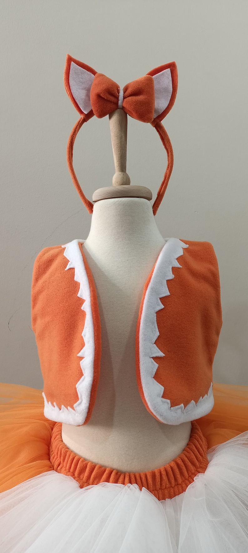 May include: Orange and white fox costume for a child, featuring a tutu skirt, a vest with a white trim, and a headband with fox ears and a bow.