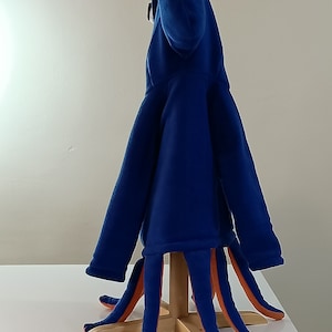 May include: A blue fleece octopus costume with orange tentacles. The costume is on a wooden stand.