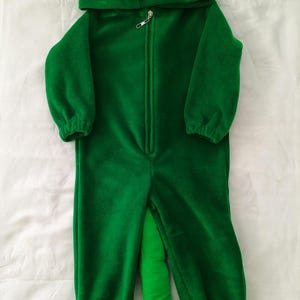 May include: Green fleece hooded jumpsuit with a long tail, designed to look like a chameleon. The hood has large, cartoon eyes and a textured spine.