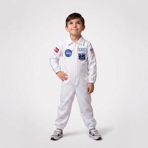 Może przedstawiać: Biały kostium astronauty z naszywkami NASA i flagi amerykańskiej. Kostium ma zamek błyskawiczny z przodu, długie rękawy i kołnierz. Dziecko ma na sobie szaro-niebieskie trampki. Kostium jest przeznaczony dla dzieci.