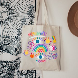 May include: A beige tote bag with a rainbow, eyes, and a bee design. The bag has the text "#LOVEWINS!" printed on it.