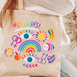 May include: A beige tote bag with a rainbow, a sun, a star, a bee, and the text "#LOVEWINS!" and "JUST BEE YOURSELF!" printed on it.