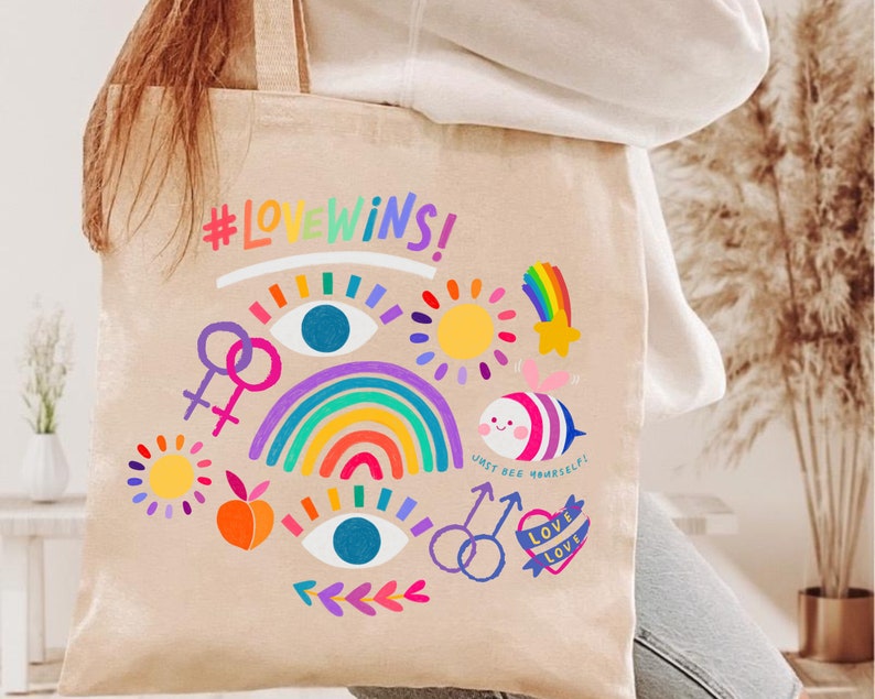 May include: A beige tote bag with a rainbow, a sun, a star, a bee, and the text "#LOVEWINS!" and "JUST BEE YOURSELF!" printed on it.