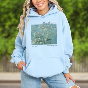 A woman wearing a light blue hoodie with a graphic of a tree with yellow flowers on it.