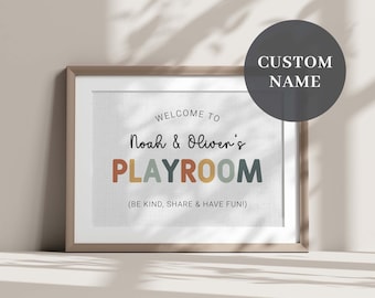 May include: A framed print with a white background and brown frame. The print says "Welcome to Noah & Oliver's Playroom (Be kind, share & have fun!)" in black text. The word "Playroom" is in colorful letters.