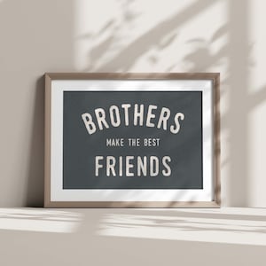 Może przedstawiać: Wydruk w ramie z ciemnoniebieskim tłem i białym tekstem, który brzmi "Brothers make the best friends". Rama jest wykonana z jasnego brązowego drewna.