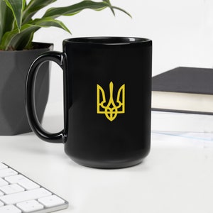 May include: A black ceramic mug with a gold Ukrainian trident symbol on the front.