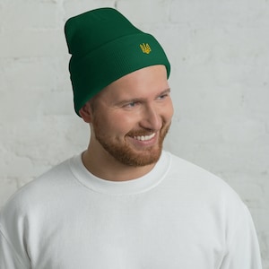 May include: A dark green beanie with a gold embroidered Ukrainian trident symbol.