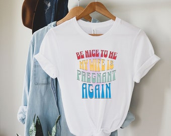 May include: White t-shirt with a rainbow-colored graphic that says "Be nice to me my wife is pregnant again".
