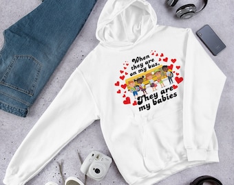 以下が含まれることがあります： バスに乗っている子供たちのグラフィックと「When they are on my bus, They are my babies」というテキストがプリントされた白いパーカー。
