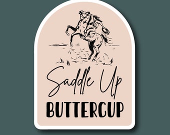 May include: A sticker featuring a black and white illustration of a cowboy riding a bucking horse. The text "Saddle Up Buttercup" is beneath the illustration.