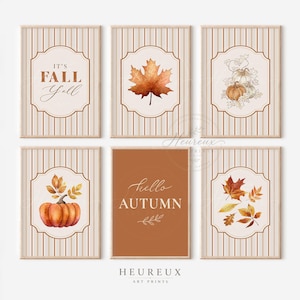 May include: A set of six rectangular wall art prints featuring autumn themes. Five prints have beige vertical stripes and central frames containing watercolour illustrations of pumpkins, maple leaves, and the text IT'S FALL Y'ALL. One print is solid orange with the text hello AUTUMN.