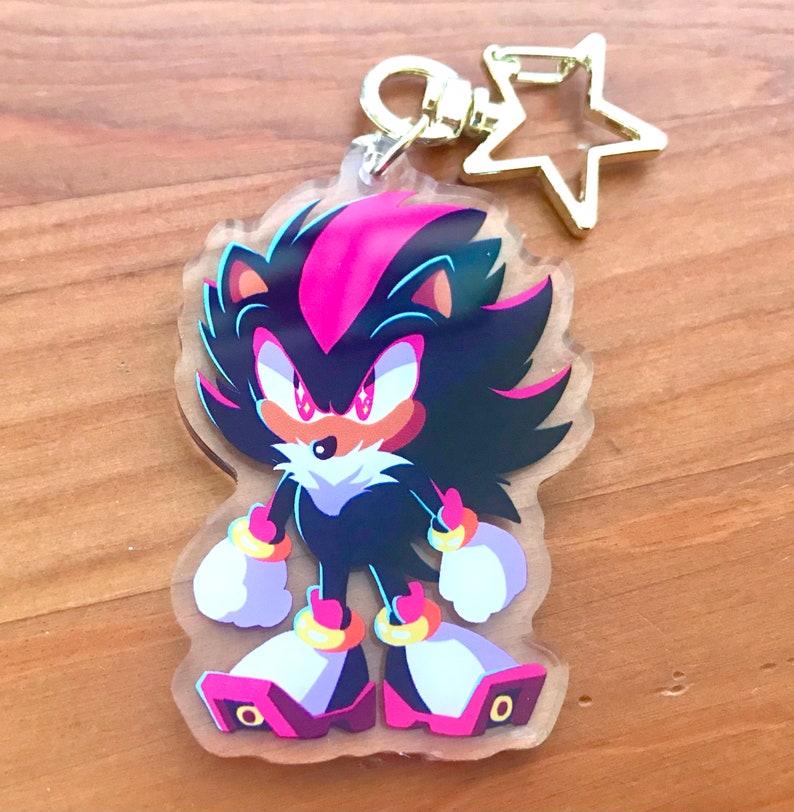 May include: A black and pink anime character keychain with a gold star charm. The character has red eyes, a black and pink mohawk, and is wearing gold rings on its wrists.