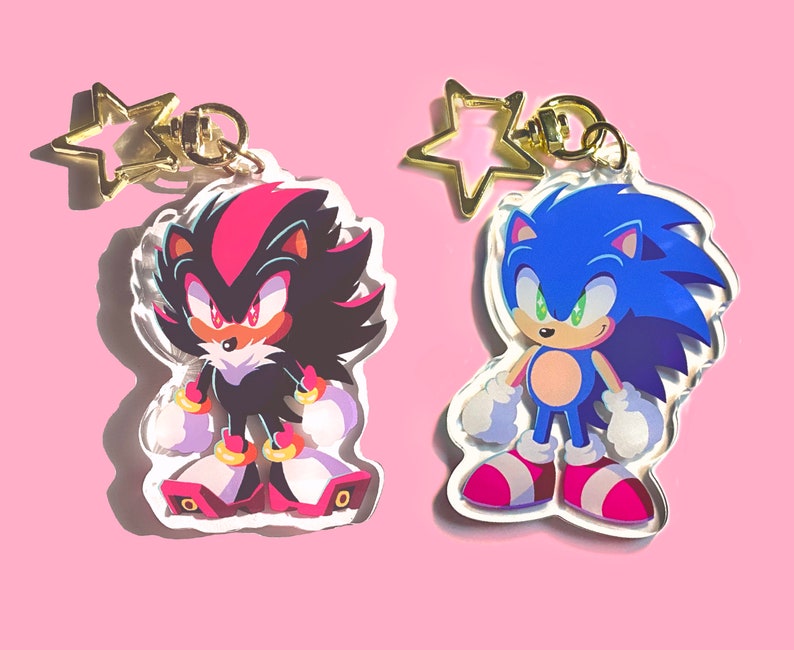 May include: Two character keychains featuring Sonic the Hedgehog and Shadow the Hedgehog. Sonic is blue with a red and white shoe. Shadow is black with red eyes and a red and white shoe.