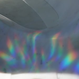 K&ouml;nnte beinhalten: Abstraktes Bild einer gew&ouml;lbten, grauen Oberfl&auml;che mit Regenbogenlichtreflexionen. Das Licht erzeugt Farbstreifen, darunter Rot, Orange, Gelb, Gr&uuml;n, Blau und Violett, &uuml;ber die Oberfl&auml;che. Der Gesamteffekt ist ein Spiel von Licht und Farbe.