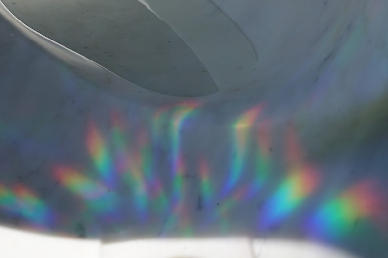 K&ouml;nnte beinhalten: Abstraktes Bild einer gew&ouml;lbten, grauen Oberfl&auml;che mit Regenbogenlichtreflexionen. Das Licht erzeugt Farbstreifen, darunter Rot, Orange, Gelb, Gr&uuml;n, Blau und Violett, &uuml;ber die Oberfl&auml;che. Der Gesamteffekt ist ein Spiel von Licht und Farbe.